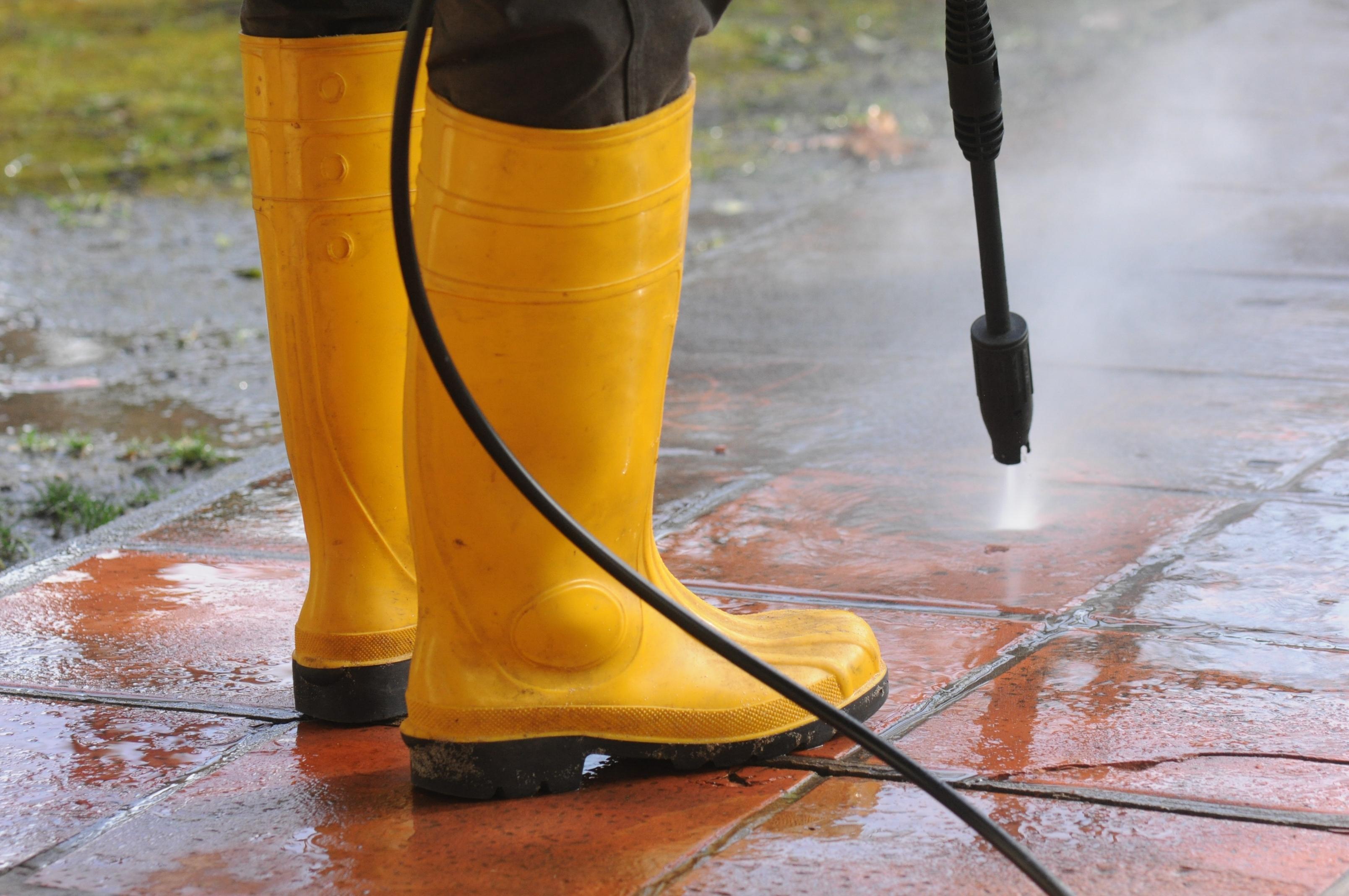 person-wearing-yellow-rubber-boots-with-high-pressure-water-nozzle-cleaning-dirt-tiles (1)(1)